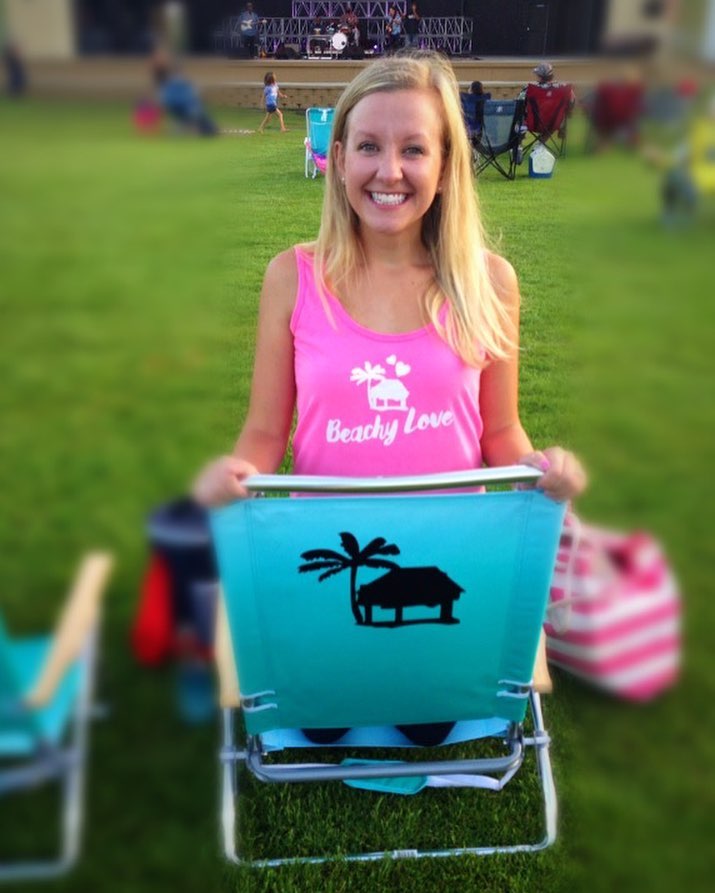 A woman smiling while showing off her beautiful teal Beachy Beach beach chair while waiting for the next performer.